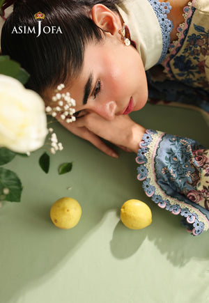 Asim Jofa AJUBC-07 printed lawn campaign portrait – model resting on a table, with blue floral cuff beside yellow lemons